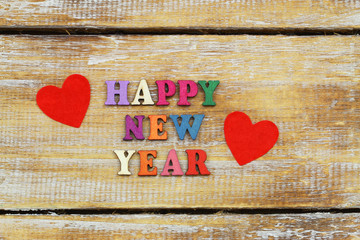 Happy New Year written with colorful wooden letters on rustic surface and two red hearts
