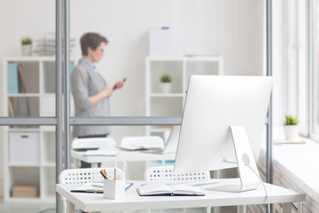 Workplace of employee by transparent board with office worker behind