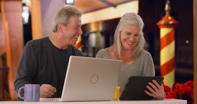 Caucasian man and his wife browse the internet at outdoor coffee shop at night