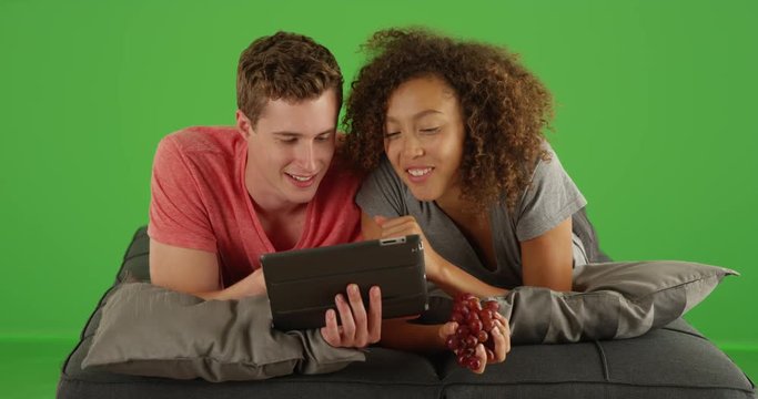 Cheerful couple using digital tablet on couch on green screen. On green screen to be keyed or composited. 