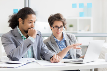 Confident employee making presentation and pointing at data on laptop display while explaining it...