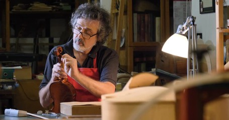 The professional violin master makes a violin with his own hands, uses a clean tree spruce, pine, glasses, planes, tunes strings. Concept: spiritual instrument, hand made, art, music, melody, sound. - Powered by Adobe