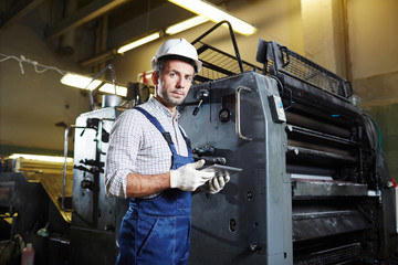 Young worker in uniform, gloves and helmet searching for online advice how to repair industrial...