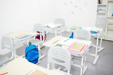 Desks with school supplies with chairs near by in empty classroom at break