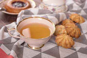 Cake in white plate, napkin, butter dish, spoon and cup of tea on wooden table
