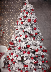 Snowy Christmas tree with red gifts decoration before bokeh lights on the wall in holiday room interior home.