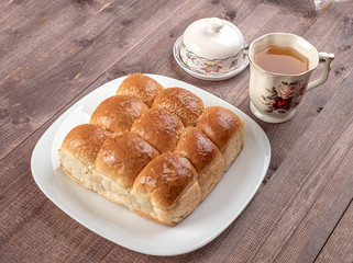 White bread in glass plate, butter dish and cup of tea on wooden table