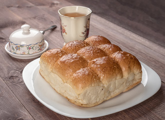 White bread in glass plate, butter dish and cup of tea on wooden table