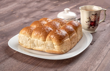 White bread in glass plate, butter dish and cup of tea on wooden table