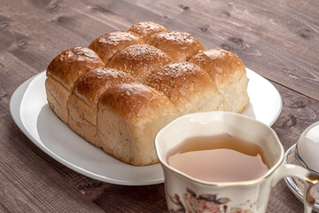 Cup of tea, white bread in glass plate, butter dish and on wooden table