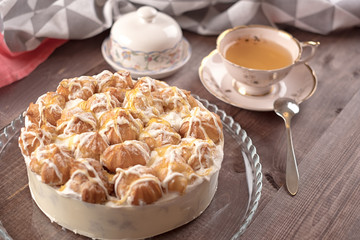 Cake in glass plate, napkin, butter dish and cup of tea on wooden table