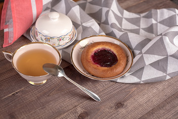 Cake in white plate, napkin, butter dish, spoon and cup of tea on wooden table