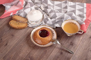 Cake in white plate, napkin, butter dish, spoon and cup of tea on wooden table