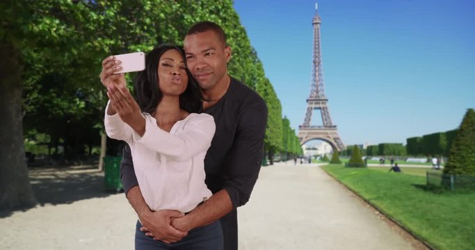 African male and female take photos of themselves near Eiffel Tower in Paris