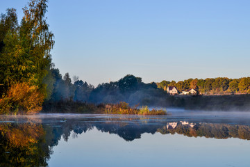 Idyllic secluded place for living in nature. Houses near a forest lake. Fog over the water. Autumn