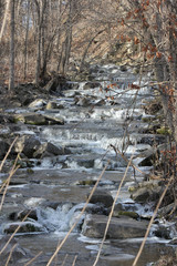 Cascading water down a slight hilly and rocky incline. Ice beginning to form on rocks at the beginning of the winter season.  