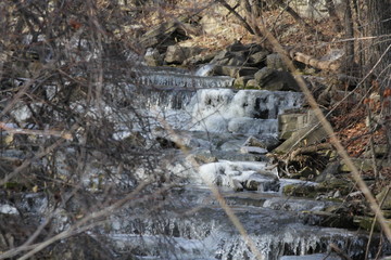 Cascading water down a slight hilly and rocky incline. Ice beginning to form on rocks at the...