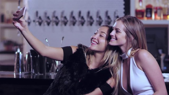 Two young attractive woman taking a selfie at a bar. They keep on talking, and consuming their alcoholic drinks afterwards 