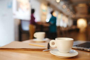 White porcelain cup on saucer and business supplies on one of tables in cafe