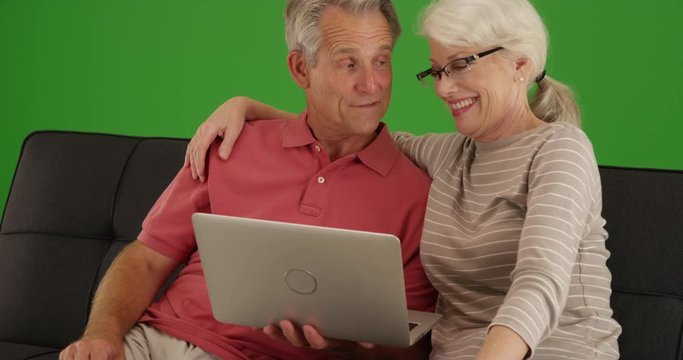 Cute elderly couple using laptop together at home on green screen. On green screen to be keyed or composited. 