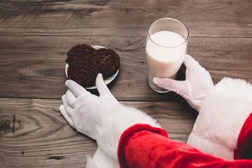 Close up of Santa's hands picking up cookies and milk left on the table on Christmas Eve