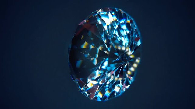 The diamond is rotation and shimmer all the colors of the rainbow when it hits the rays of light. Isolated on blue and black background. Macro. Closeup

