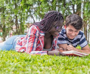 Multi etnic teenagers couple relaxing with school books on the grass