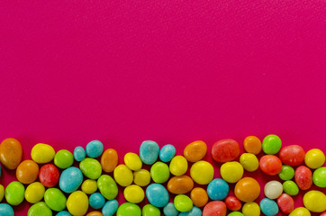 Multicolored candy on pink background with space for text
