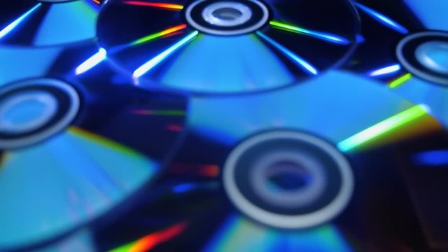 Many compact discs lying on top of each other rotate and shimmer in different colors. Macro. Closeup. Shallow depth of field. Jib arm
