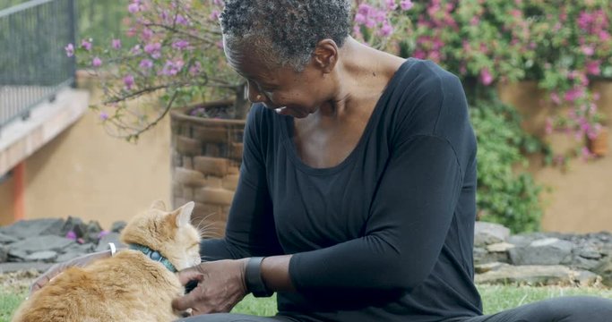 Beautiful elderly black woman petting her orange cat with love outside