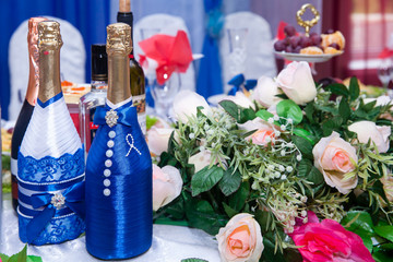 two decorated bottles of champagne for the bride and groom on the wedding table with beautiful roses