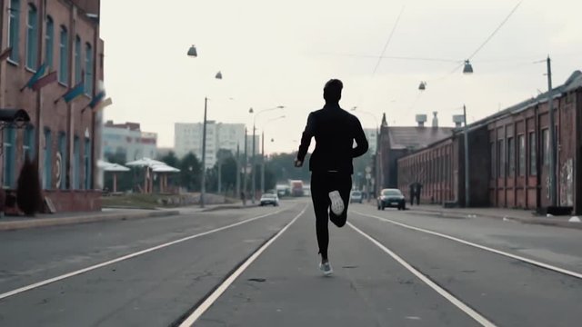 Man running fast in the middle of an old street. Real time shot. Freedom. Camera follows sportsman between tram tracks.