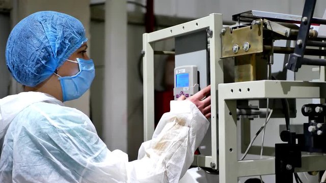 Employee worker woman in masked and protective gown operating control panel of the machine and controls the packaging machine for packing chemicals or any powders on factory