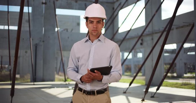 Portrait of handsome young contractor at construction site holding tablet