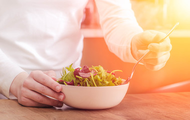 Woman is cooking and eating fresh delicious green salad with vegetables broccoli, spinach, lettuce, chard, parsley, cucumber, arugula.  