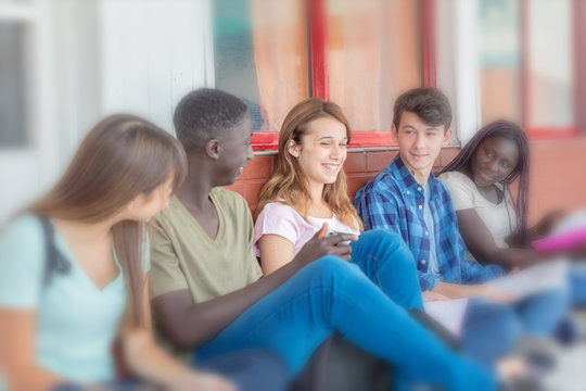 Group Of Teenagers Smiling Seated In School Entrance Corridor