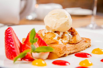 Apple pie with ice-cream decorated with a strawberry, fruit sauce and herb served in a restaurant
