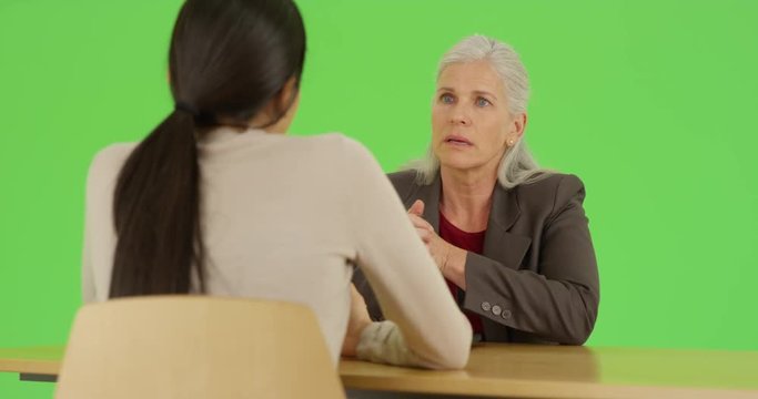 An experienced businesswoman interviews a young new prospect on green screen. On green screen to be keyed or composited. 