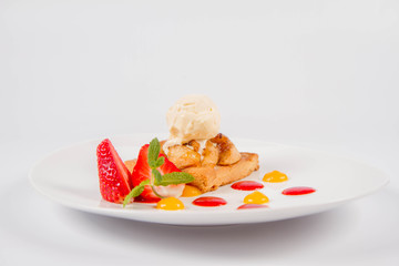 Apple pie with ice-cream decorated with a strawberry, fruit sauce and herb on a white background