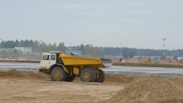 Large quarry dump truck rides, driving on construction site. Concreting of airport runways roads, highway. Construction machinery works on runway construction of national airport Minsk, MSQ