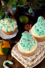 Fototapeta na wymiar Cupcakes decorated with cream forming Christmas fir trees on a wicker basket surrounded by festive attributes on a wooden table