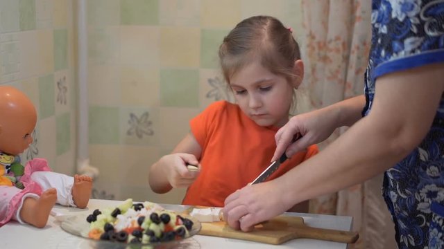Little cute girl and her grandma is cut the cheese to prepare a salad.