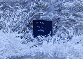 Happy New Year text on black card with silver beads on white fluffy background