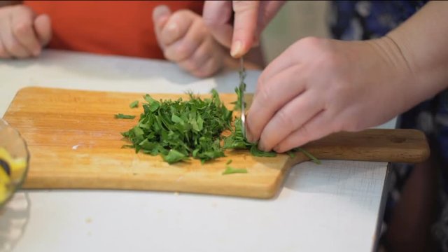 Woman cuts parsley for prepare a salad on a cutting board close-up.