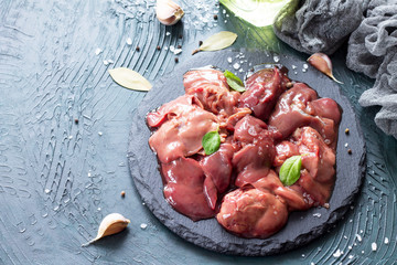 Raw chicken liver on a slate board and spices on a stone with a gray stone background.