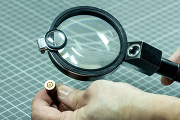 A forensic service officer holds in his hand a magnifying lens and a cartridge from the firearm and will conduct a ballistic examination. Close-up.