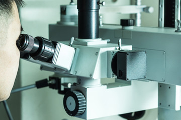A man looks into the eyepieces of magnifying equipment. Professional laboratory microscope.