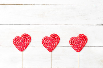 Three candies on a stick in the shape of a heart on a wooden background. Copy space