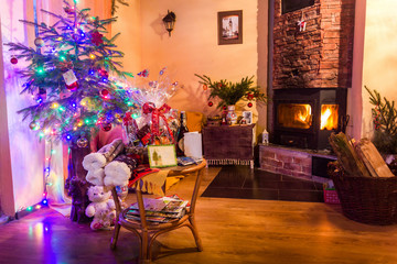 A living room lighted with numerous lights decorated ready to celebrate Christmas. Christmas tree decorated by lights and garland lighting indoors fireplace.