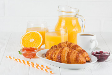 Freshly baked croissant, orange juice, fresh fruits, jam on white wooden background. French breakfast. Fresh pastries for morning. Delicious dessert. Closeup photography. Horizontal banner